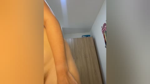 Video of a narrow, beige-walled hallway with a wooden closet on the right. A person with a fair skin tone, possibly female, is partially visible, bending to the left.