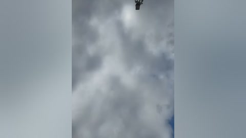Video of a cloudy sky with scattered, white and gray clouds, and a small, dark object (possibly a bird or a small aircraft) in the upper left corner. The sky is overcast with a muted, dreary color palette.