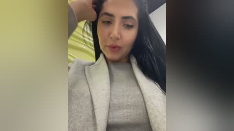 Video of a young woman with long black hair, light brown skin, and medium build, wearing a gray sweater, lying on a yellow bedspread.