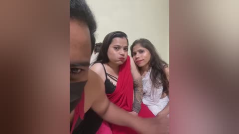 Video of two young South Asian women, one with long black hair in a red saree, the other with long brown hair in a white top, both with tattoos.