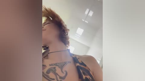 Video of a woman with curly, auburn hair wearing a camo halter top, revealing a large tattoo on her left shoulder. Background features a modern, minimalist interior with white walls and recessed lighting.
