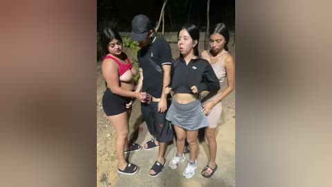 Video of four young women and one man, outdoors at night, in casual attire, with one woman topless, exposing her breasts.