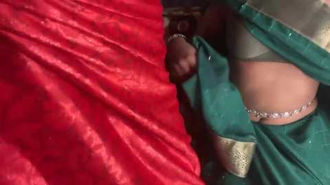 A video showing a woman in a red saree and green blouse, with a silver anklet and black watch.