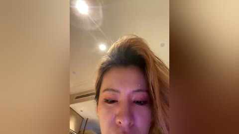 A video of an Asian woman with light skin, brown hair, and heavy makeup, including dark eyeliner and red lipstick, taken indoors with ceiling lights.