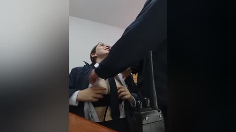 Video of a woman in a dark suit, kneeling with her head tilted back, holding a man's foot in submission, in a dimly lit room.