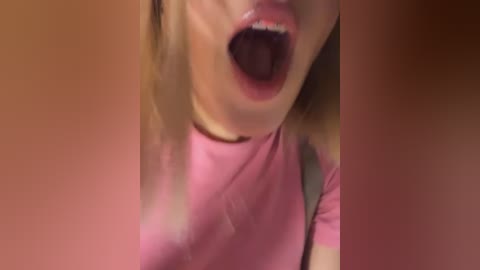A video of a young woman with light skin and blonde hair, wearing a pink t-shirt, mid-scream with saliva drooling from her open mouth.