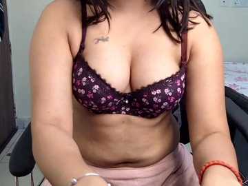 Video of a light-skinned woman with dark hair wearing a purple floral bra and a pink skirt, sitting in a chair with a tattoo on her upper arm.