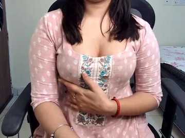 Video of a light-skinned woman with shoulder-length dark hair wearing a pink, polka-dotted dress with a floral-patterned front, sitting in an office chair. She covers her belly with her hands.