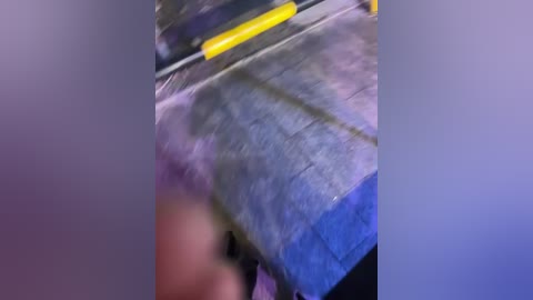 Video of a blurred, dark-skinned hand holding a blue fabric, possibly a shirt, against a purple backdrop. The hand's fingers are slightly out of focus, adding a dynamic, motion blur effect.