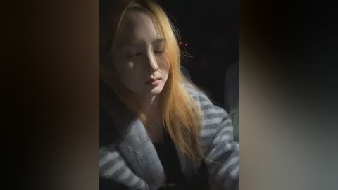 Video of a young woman with long, straight blonde hair, wearing a grey and white striped sweater, eyes closed, looking contemplative.