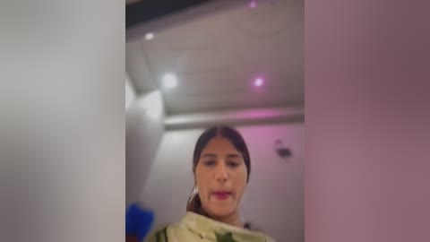 A video of a young woman with dark hair and fair skin, wearing a beige and green sari, captured indoors with blurred background, hinting at a modern, possibly clinical setting.