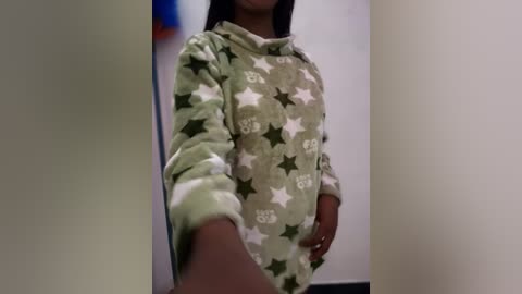 Video of a young person wearing a light green, star-patterned hoodie with long sleeves, standing indoors against a plain white wall.