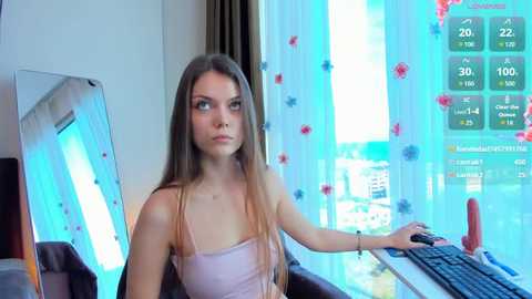 Video of a young Caucasian woman with long brown hair, wearing a light pink spaghetti-strap top, sitting at a desk in a modern room with a blue-tinted window and virtual reality headset.