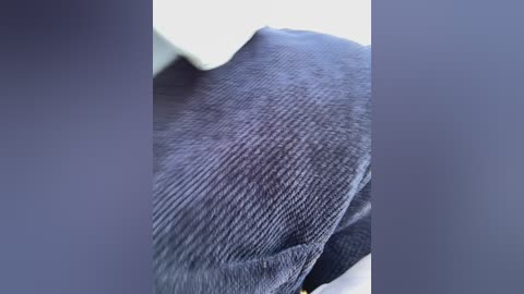 Video of a close-up view of a dark gray, textured wool sweater with a smooth, slightly wrinkled surface. The sweater appears to be draped over a white surface, possibly a table or couch.