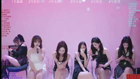 Video of five Asian women with long hair, dressed in black and white, sitting on transparent chairs against a pink background, looking at smartphones, captioned in Chinese.