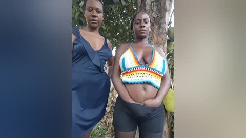 Video of two African women standing outdoors. One wears a navy blue dress, the other a colorful, crochet bikini top and black shorts. Background features lush green foliage.