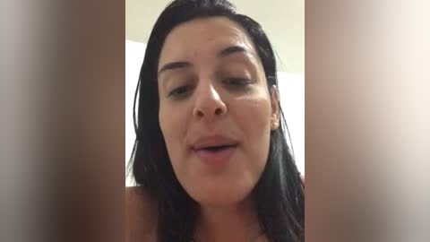 A close-up video of a smiling woman with dark hair, light skin, and subtle makeup, captured from a slightly angled perspective, with blurred background.