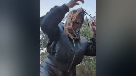 A video of a woman in a black leather jacket, holding a long, dark braid with her hands, against a blurred green background.