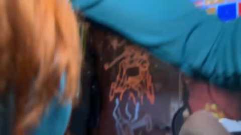 Media: A blurred video of a person's face partially covered by a green hat, revealing a tattoo of a spider web on the chest.