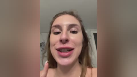 A video of a smiling young woman with light skin, brown hair, and a slight gap between her teeth, wearing a light-colored top, captured from a close-up angle.