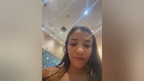 Media: Video of a young woman with long, dark hair, light skin, and dark eyes, taken in a brightly lit, modern indoor setting.