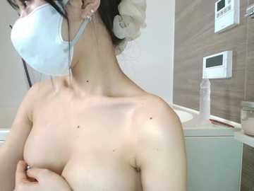 Video of a topless woman with light skin, wearing a white face mask, with dark hair tied up, in a bathroom with a white sink, mirror, and thermostat.
