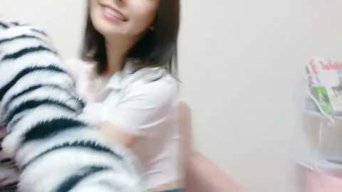 A video shows a smiling Asian woman with straight black hair, wearing a white and black striped shirt, hugging a person from behind, blurred in the foreground.