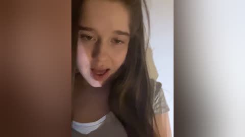 Video of a young woman with long dark hair, light skin, and a neutral expression, partially hidden by a person's hand, possibly in a playful or intimate setting.