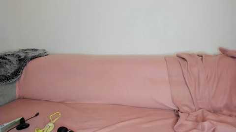 A video of a pink mattress with a dark gray blanket on a light gray carpet. The bed appears unmade, with a black and white patterned pillow visible on the left.