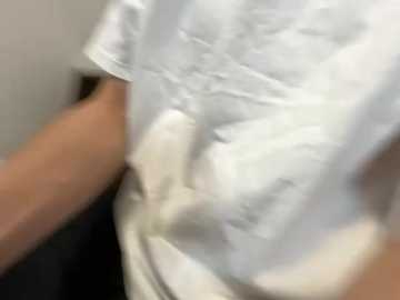 A close-up video of a person's upper body wearing a white T-shirt. The shirt is slightly wrinkled and the individual's right arm is visible, with a tattoo partially visible on the forearm. The background is blurred, focusing attention on the garment.