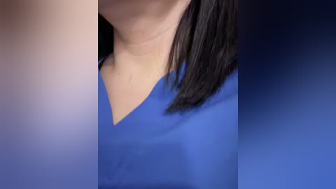 A close-up video of a woman's upper torso, wearing a bright blue medical scrub top with a deep V-neck. The background fades from dark blue to light blue, emphasizing the uniform. Her straight, shoulder-length black hair partially obscures the neckline.