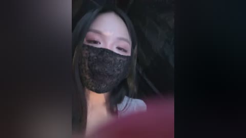 Media: A video of a young Asian woman with long black hair, wearing a black lace mask and dark, heavy makeup. The background is dark and blurry, creating a mysterious, eerie atmosphere.