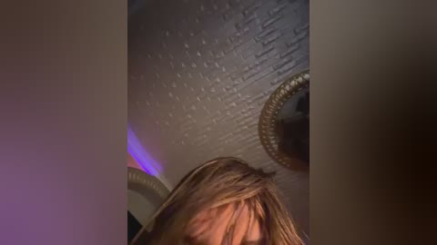 Video of a person with light brown hair, partially obscured, standing under a textured ceiling with a circular light fixture.