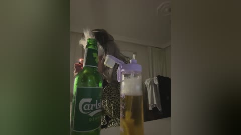 Video of a woman in a leopard-print dress spraying beer into a plastic bottle. Background shows a dimly lit, cluttered room with a hanging jacket.