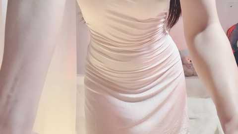 A video of a woman's back in a tight, light pink dress, showcasing her curvy figure and smooth skin, with a blurred background of soft lighting and indistinct objects.