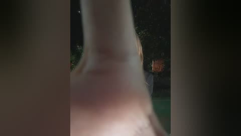 A dimly-lit video features a blonde woman in a white dress, partially obscured by tree trunks. In the background, a man with orange hair stands in a green field, partially visible.