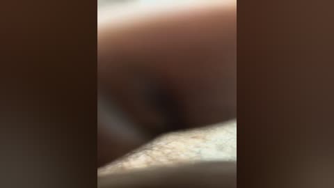 A close-up video of a human vulva, blurred with brown and beige tones, showing the labia and surrounding skin. The image lacks fine details due to the blur, making it difficult to discern specific anatomical features.