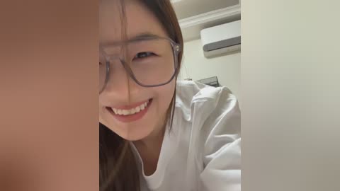 Media: Video of an Asian woman with glasses, smiling, wearing a white lab coat in a medical setting, with an air conditioner in the background.