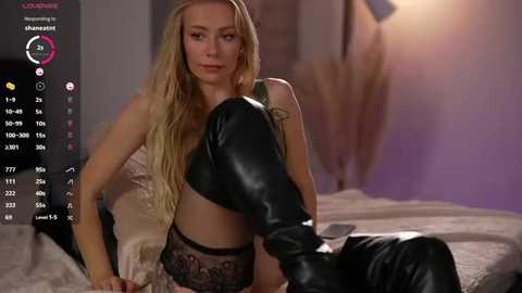 A video of a blonde woman in black leather thigh-high boots, revealing lingerie, sitting on a bed in a dimly lit room.