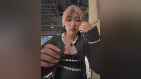 A video shows a young Asian woman with light skin and pink hair, wearing a black lace dress with white frills. She has a neutral expression and is standing in a dimly lit room with exposed pipes and industrial decor.