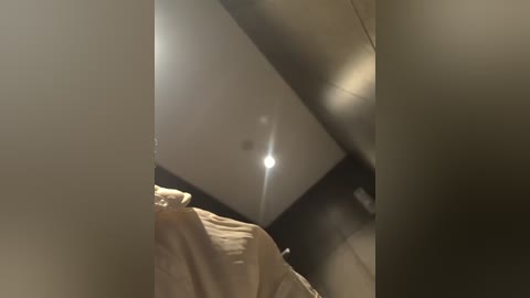 Video of a person in a dimly lit room, wearing a beige jacket, with a bright spotlight highlighting their face, creating a dramatic effect.