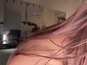 Video of a close-up view of a person's long, straight, light pink hair cascading down the right side of their face, with a mirror reflecting the room's interior, including a blue object and a white door.