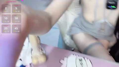 A blurred, low-resolution video shows a woman in grey lingerie with a large chest, possibly Asian, sitting at a desk. The background includes a whiteboard with a schedule and a purple surface.