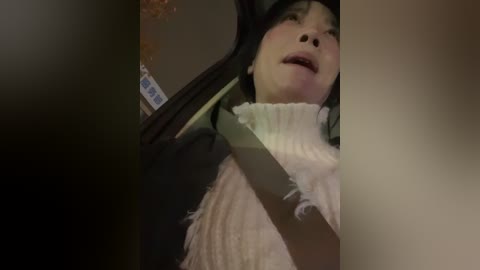 Video of an Asian man in a car, wearing a dark jacket and light scarf, mouth open, blurred background.