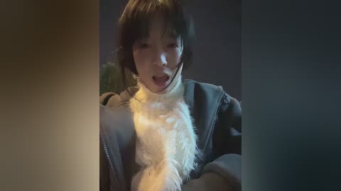 A video of a young Asian boy with short, dark hair, wearing a dark jacket and a white scarf, looking startled, against a dimly lit background.