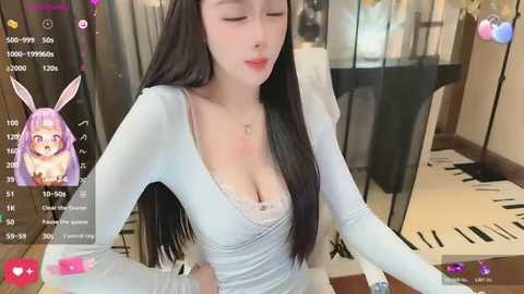 A video of an Asian woman with long, straight black hair and light skin, wearing a white V-neck top, standing in a modern room with a piano and glass window.