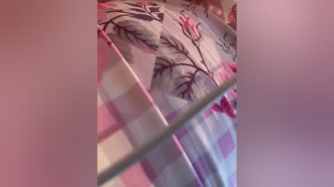 Video of a bed with a pink and white checkered sheet adorned with a floral pattern featuring red and green leaves. The image is slightly blurry, focusing on the texture and color of the fabric.