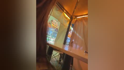 Video of a small, cozy room with a warm, dimly lit ambiance. A large window showcases a vibrant, colorful cityscape at night. The room's walls are adorned with brown curtains, and the floor appears to be wooden.