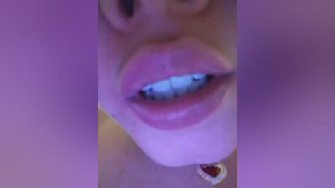 A close-up video of a woman's face, focusing on her full, glossy lips painted in a bright pink lipstick. The background is blurred, suggesting an indoor setting with a purple hue.