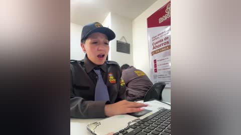 Video of a young boy in a police uniform, smiling, at a desk, with two officers in the background.